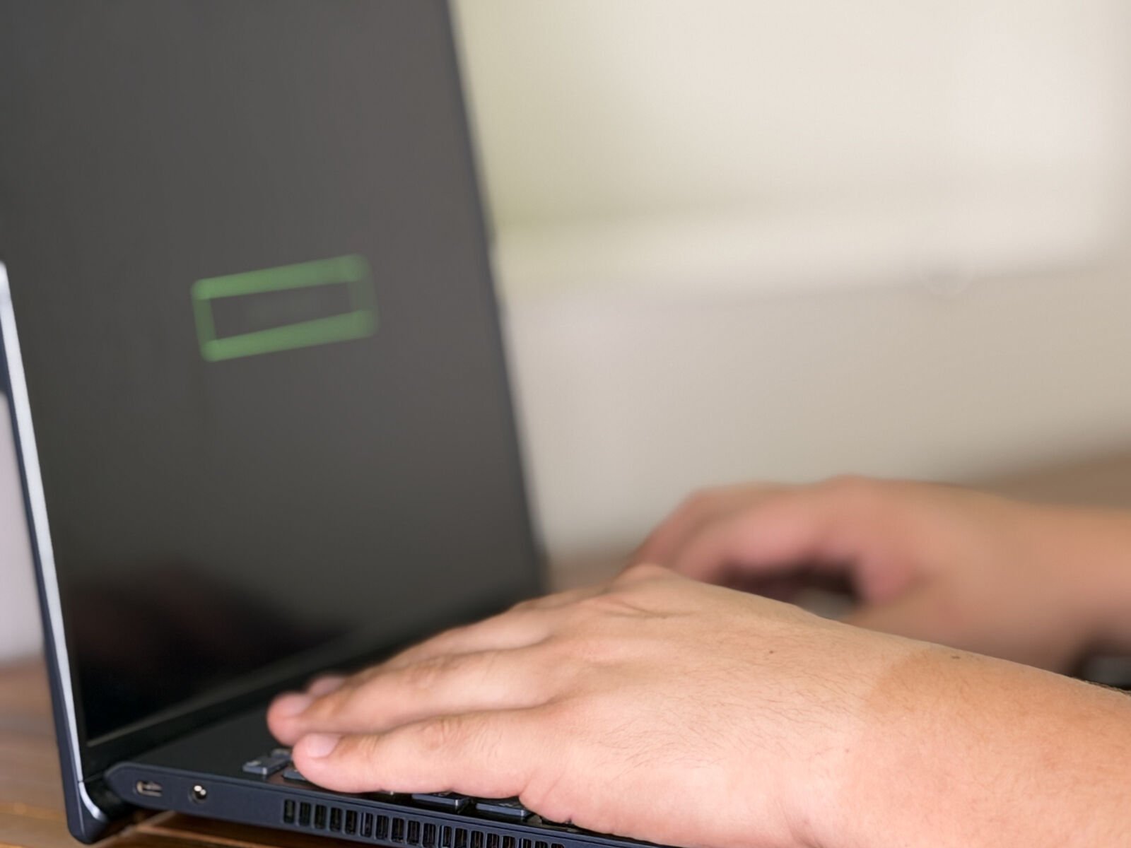 Mão sobre o teclado de um notebook aberto em uma mesa de madeira